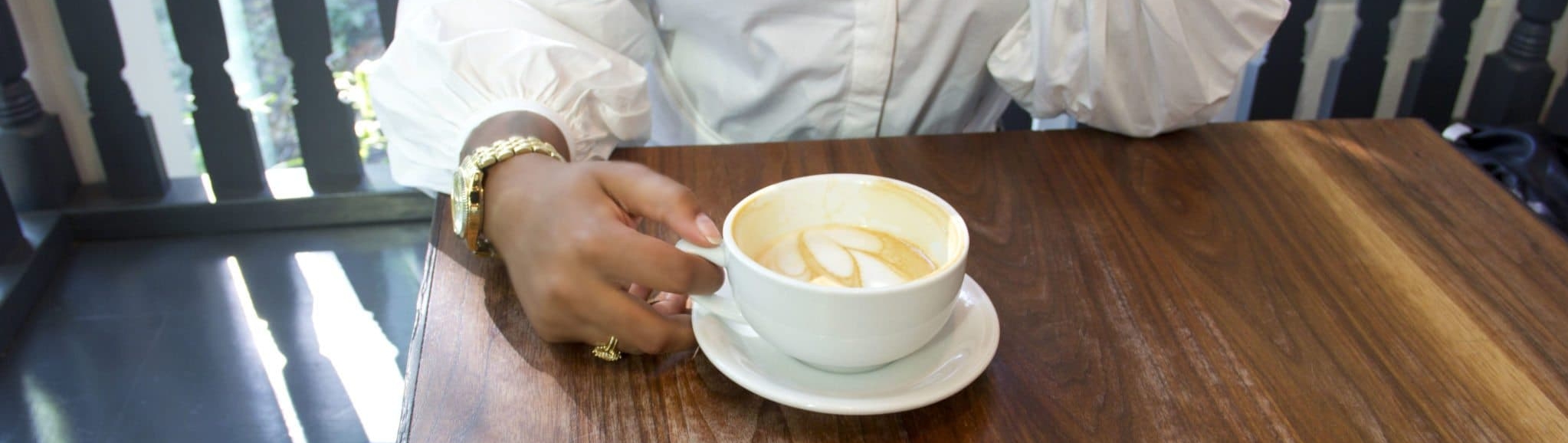 Photo (cropped) of a person sitting across the table, holding a latte. Photo credit: @marceau_photeau from nappy.co, license CC0 - thank you!"