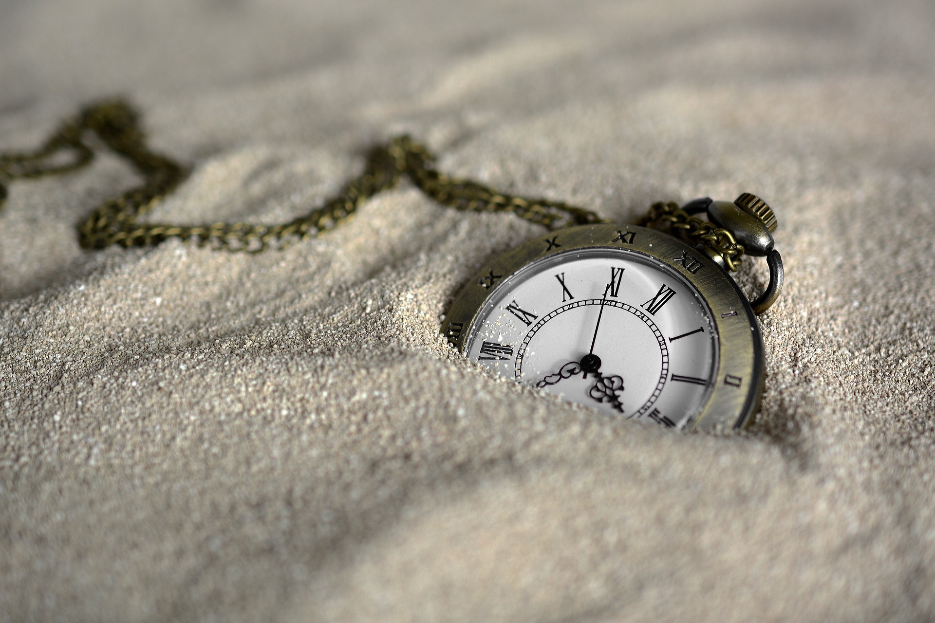 Closeup of a pocketwatch lying on a sandy beach